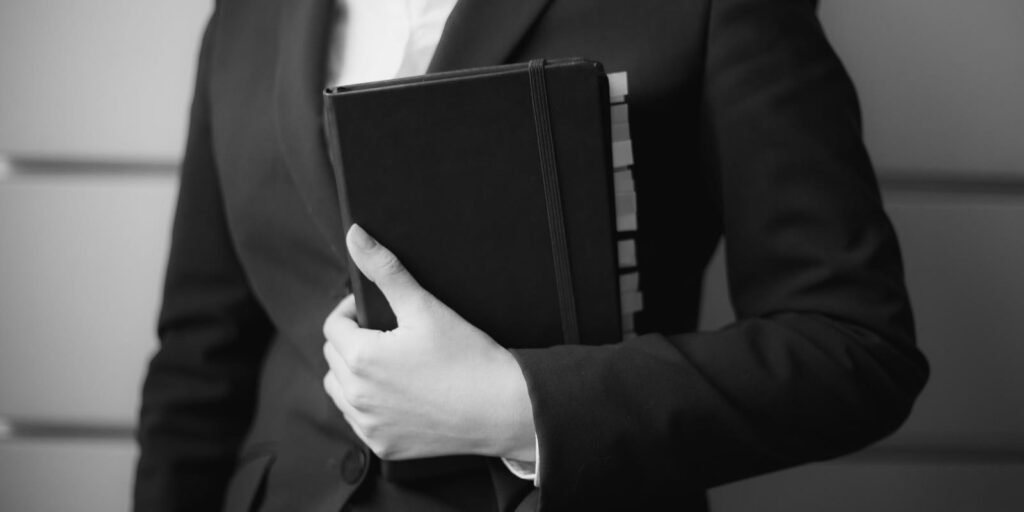 Woman in a dark suit holding a planner, black and white
