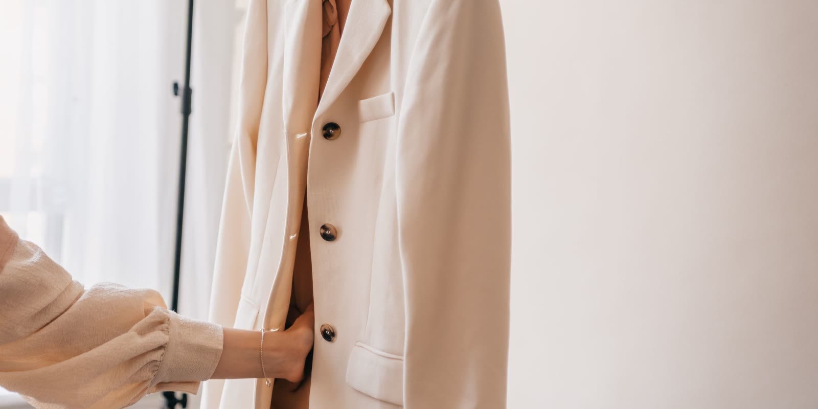 Hand touching a beige blazer on a hanger