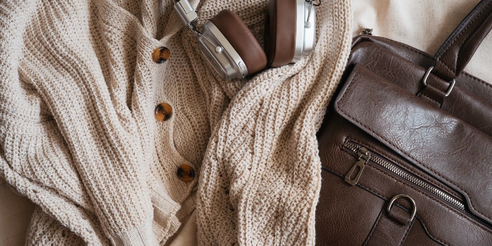 Flat lay of a cream knit, leather bag and accessories